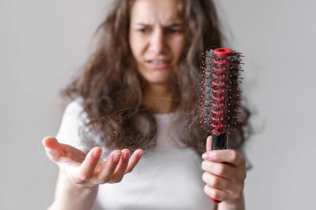 נשירת שיער. אישה מתבוננת בדאגה במסרק מלא בשערות שנשרו אחרי שסירקה את שיערה.